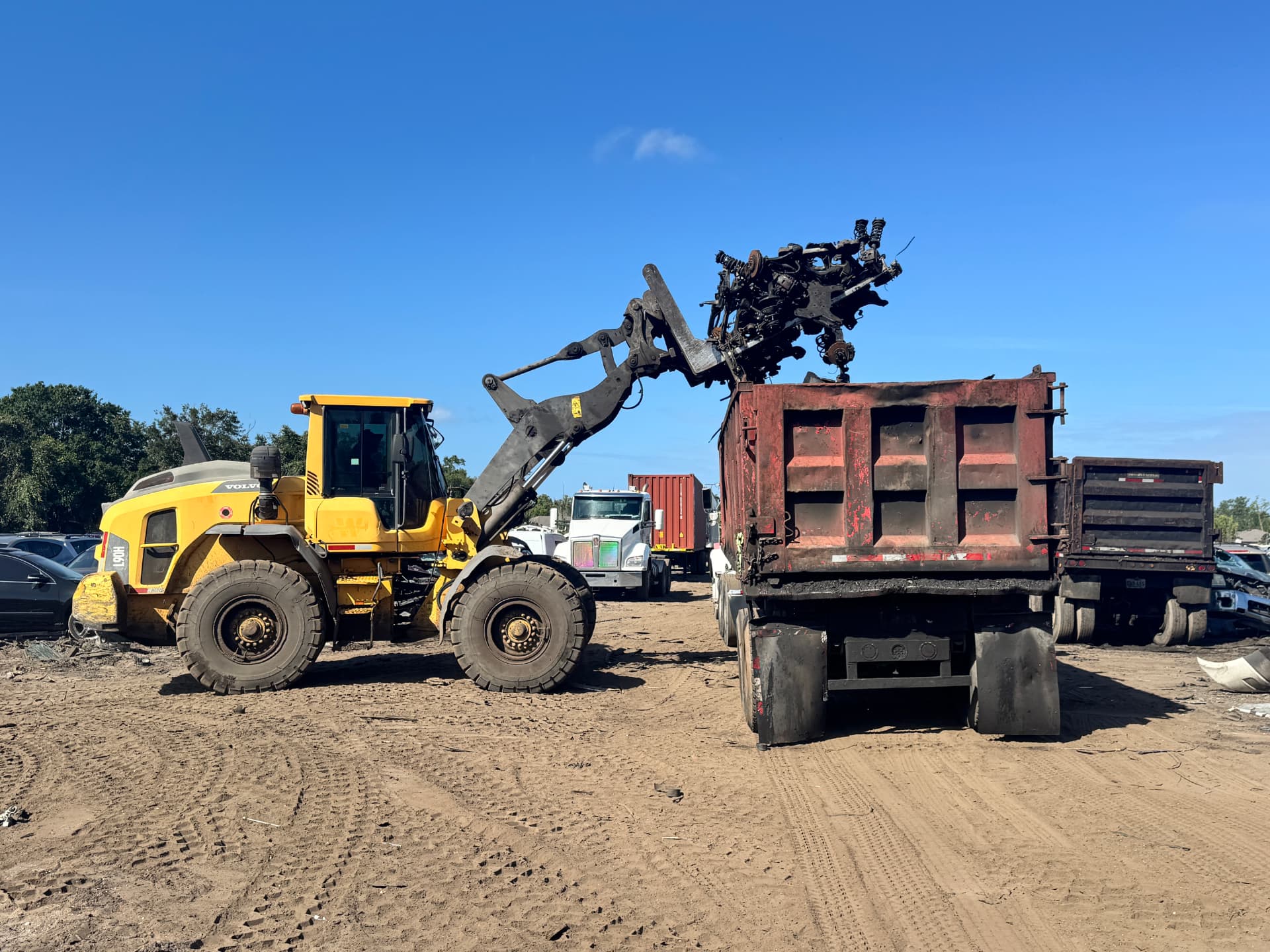Yellow loader dropping engine parts into a dumpster